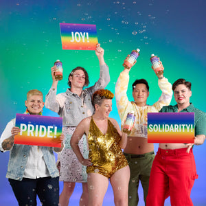 Group of people holding rainbow-colored signs with messages of joy, pride, and solidarity against a colorful gradient background.