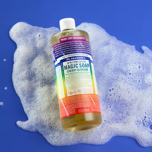 Bottle of Dr. Bronner's Limited-edition Cherry Blossom Pride Soap with rainbow label on a blue background with soap suds.