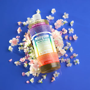 Bottle of Dr. Bronner's Limited-edition Cherry Blossom Pride Soap with rainbow label against cherry blossoms on a blue background