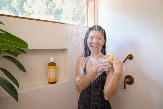 Woman in a large rainfall shower with soap suds, using Dr. Bronner's Citrus Magic Soap.